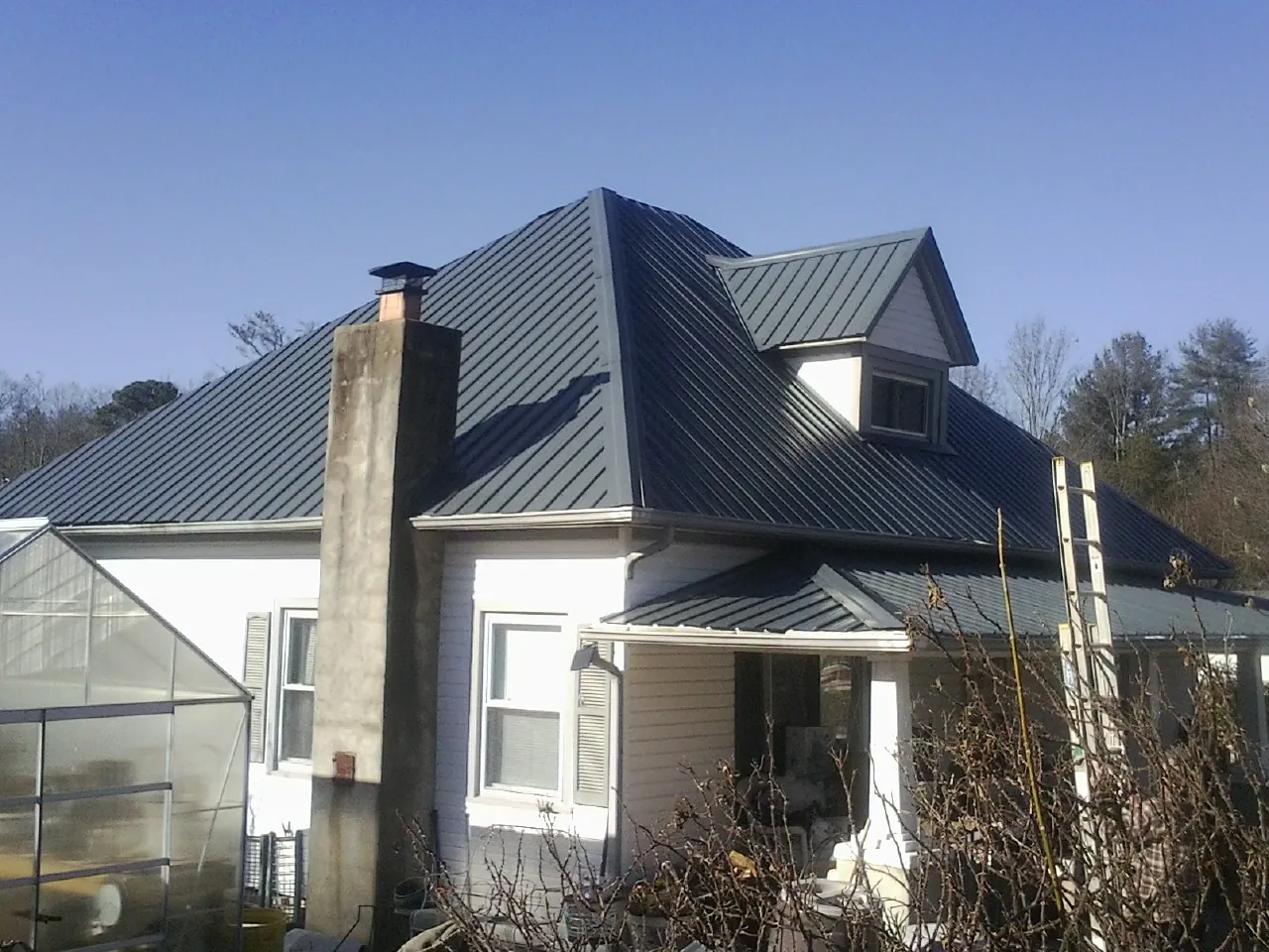 Dark blue standing seam metal roof on a white farmhouse with dormer — Slate & Tile Roof Repair by Roofing Brothers in Sulligent