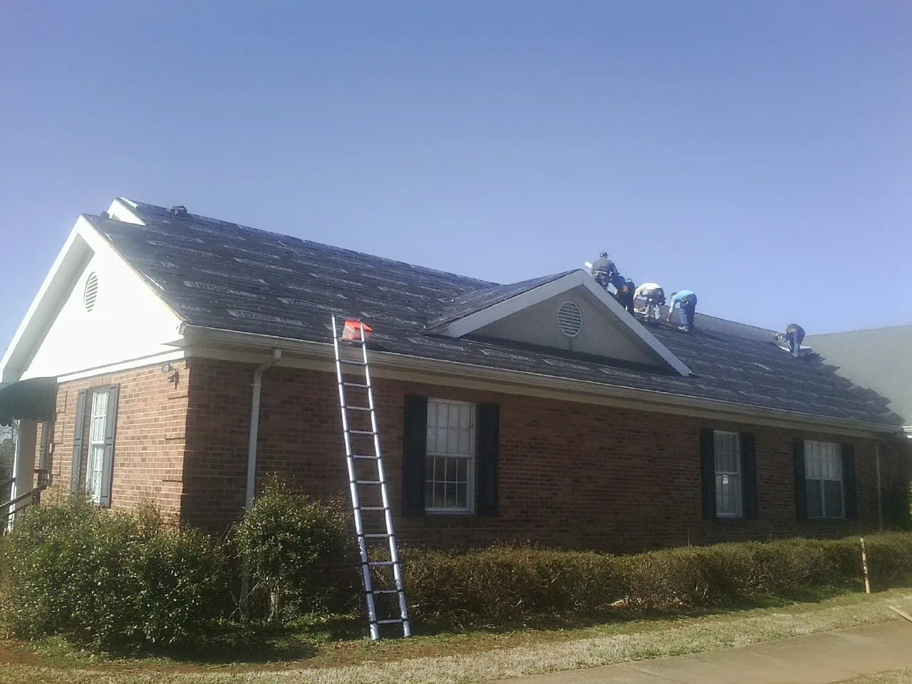 Crew tearing shingles off a brick ranch roof with a ladder set — Emergency Roof Repair work by our crew in Sulligent