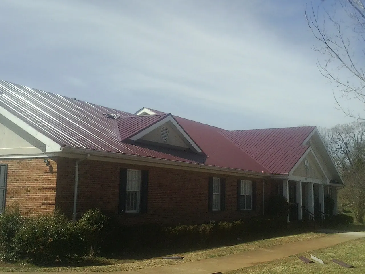 Red metal roof with gabled entries on a long brick building, from a Hail Damage Roof Repair job in Sulligent