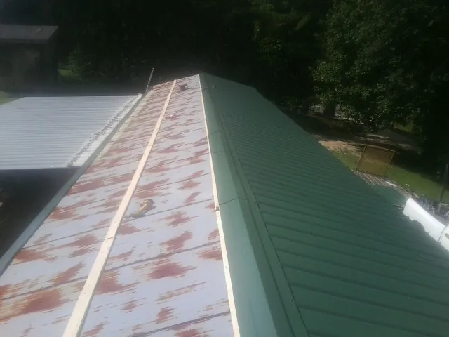 Old rusted panels beside newly installed green metal roofing — Wind Damage Roof Repair by Roofing Brothers in Sulligent